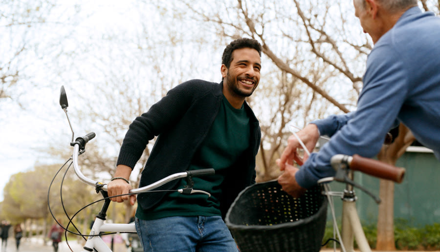 En glad man lutar sig mot sin cykel. Han ler mot en annan man som också stannat med sin cykel.