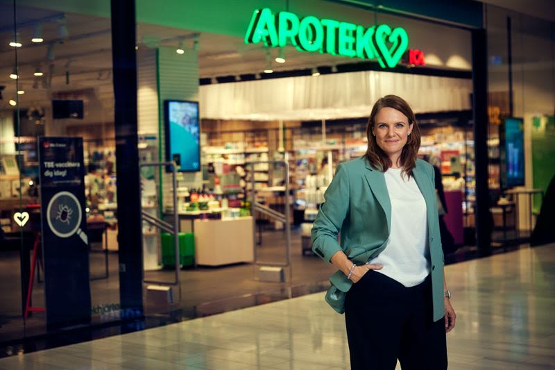 Klädd i en grön kavaj står Apotek Hjärtats VD, Monika Magnusson, utanför ett Apotek Hjärtat apotek.